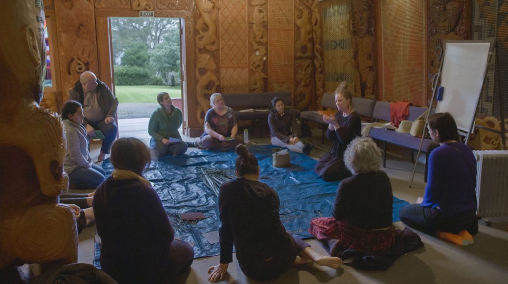 Hinekura Lisa Smith and others sit on the floor in a circle in Waiapapa Marae before beginning to weave flax into the three baskets of knowledge.